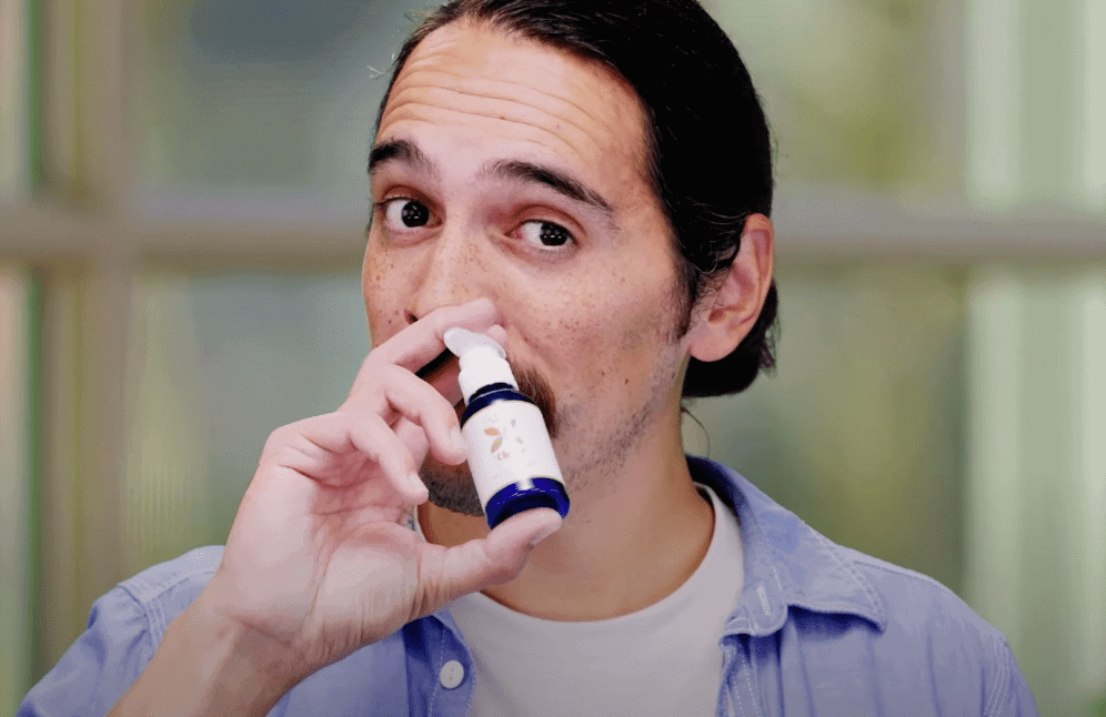 Man using a white and blue inhaler device against a blurred indoor background