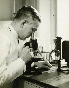 black and white photo of doctor looking into microscope