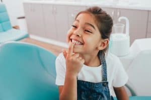 Happy little girl pointing at her healthy teeth in dentist office