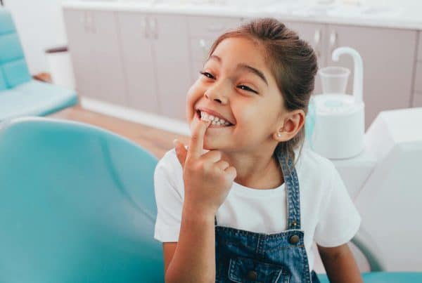 Happy little girl pointing at her healthy teeth in dentist office