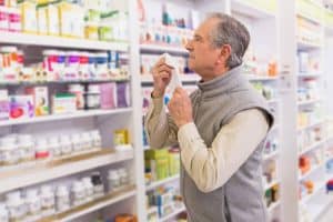 older man holding tissue looking products on pharmacy shelf
